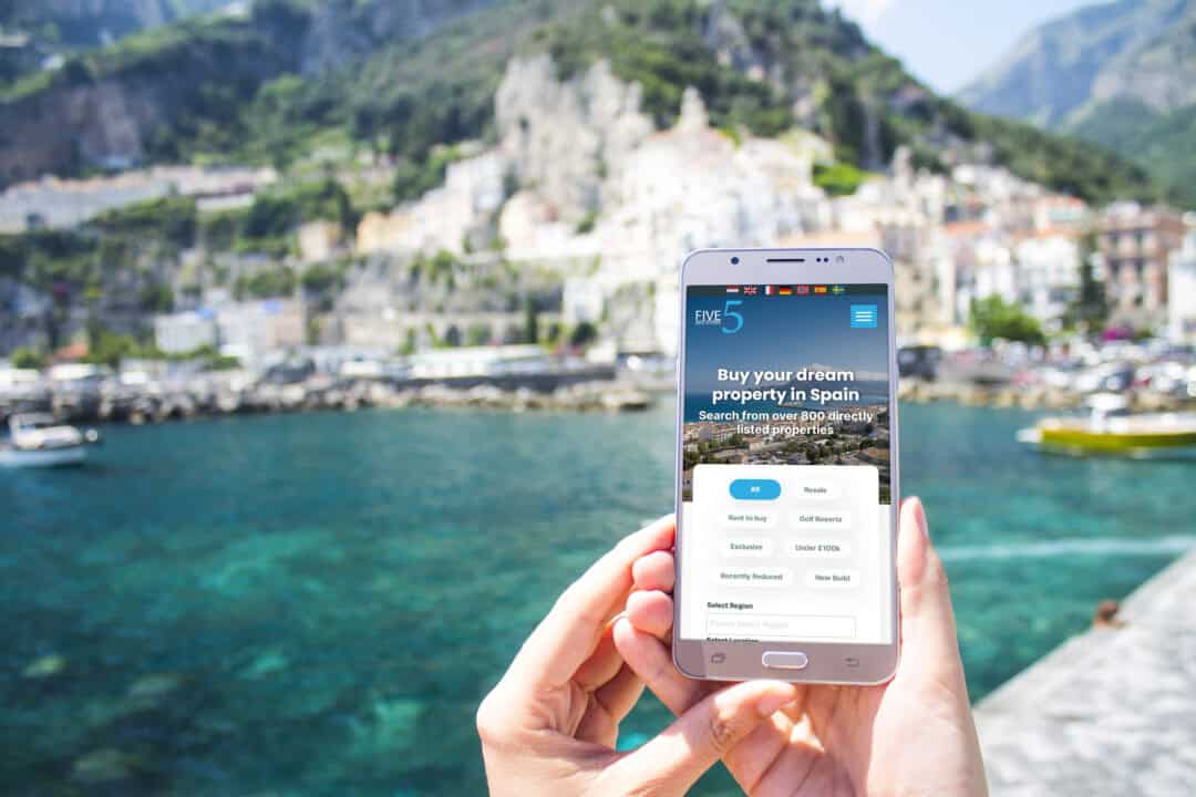 A smartphone user in a sunny Spanish location browsing the 5 Real Estate homepage